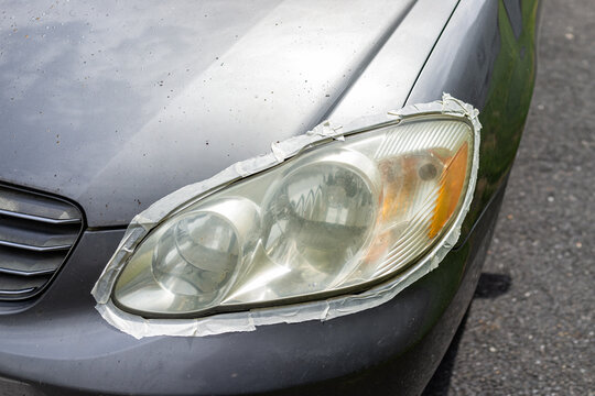Car auto vehicle front foggy dirty headlight with protective tape around light taped to protect paint for cleaning polishing at home driveway of house outside