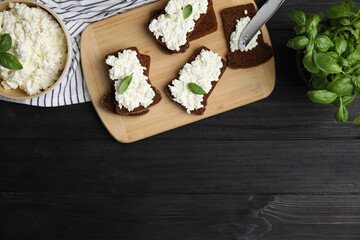 Fototapeta na wymiar Bread with cottage cheese and basil on black wooden table, flat lay. Space for text