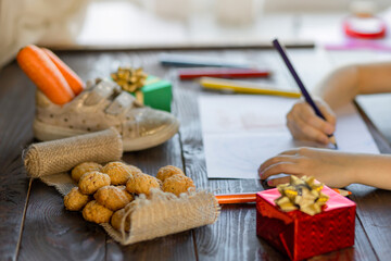 child writing letter on traditional Dutch holiday Sinterklaas. in Europe, Netherlands, Belgium girl put in in boot, shoe a carrot for Santa horse, gifts, pepernotin chocolate sweet cookies.
