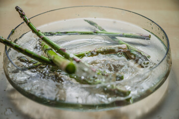 Water washing of levitating asparagus. Asparagus in a bowl of splashing water. Greenery bought at farmer's market.