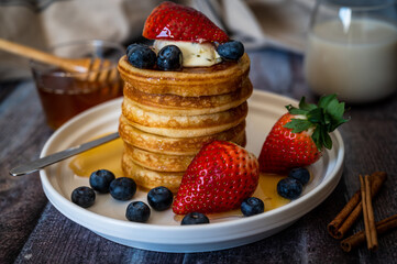 Clear view of Stack of pancakes with honey stick, strawberry, blue berry and whip cream on top in plate, delicious dessert