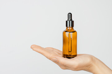 A brown bottle with a pipette in a woman's palm. Woman's hand holding a face serum