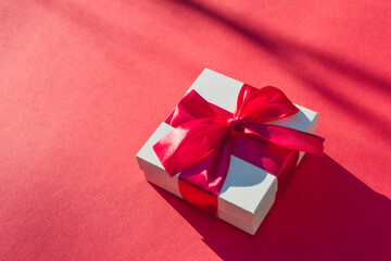 White gift box with red ribbon on a burgundy background. Valentines day backdrop. Template for banner or party invitation