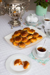 Russian traditional teaparty with samovar and pies or pirozhki with apple jam on white platter on white tablecloth 