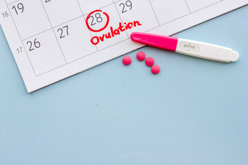 Ovulation home test and pills on calendarwith red mark