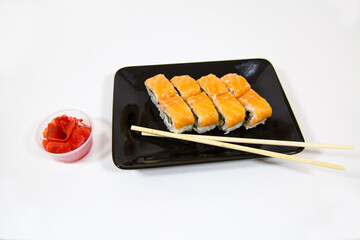 Philadelphia rolls are bright orange on a black rectangular plate with sticks isolated on a white background. Pizza traditional Japanese dishes and pastries.