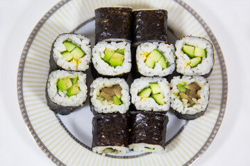 Mini rolls with cucumber and avocado on a white round plate isolated on a white background. Pizza traditional Japanese dishes and pastries.