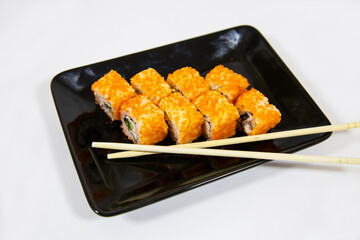 California rolls of bright orange color on a black rectangular plate with sticks isolated on a white background. Pizza traditional Japanese dishes and pastries.