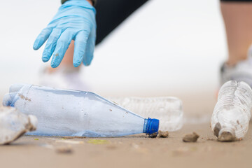 A woman volunteer's hand in a blue glove collects used plastic bottles. Concept - environmental protection, social and ecological problems. Focusing on the foreground. Close-up.