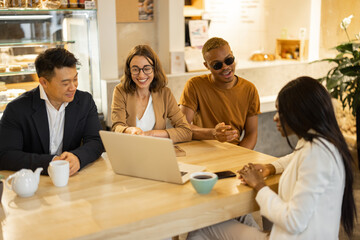 Multiracial business team talking and working in cafe or restaurant. Concept of remote and freelance work. Idea of business cooperation. People sitting at wooden table with laptop computer