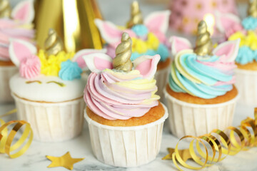 Cute sweet unicorn cupcakes and festive decor on white marble table, closeup