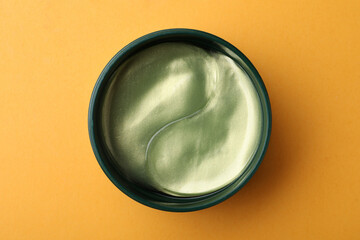 Under eye patches in jar on orange background, top view. Cosmetic product