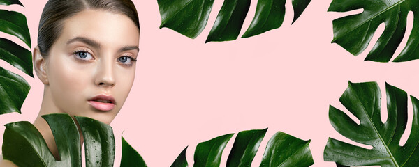 Young woman with perfect skin with tropical green leaves, isolated on pink. Beautiful fashion model with monstera plant. Concept of natural organic cosmetics, SPA, wellness and skincare procedures