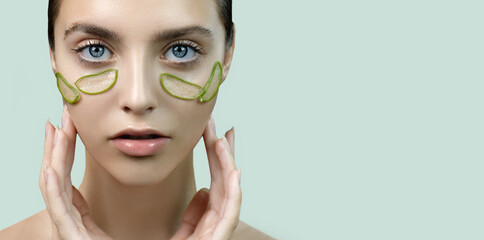 Beautiful face of young woman with few pieces of aloe vera plant on her clean perfect skin around...