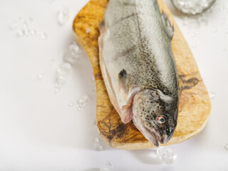 Close-up. On a white plate, one fresh fish on a cutting board. Salt is scattered nearby. Minimalism. High angle view. Cooking fish dishes. Culinary blog, advertising, restaurant, fishing.