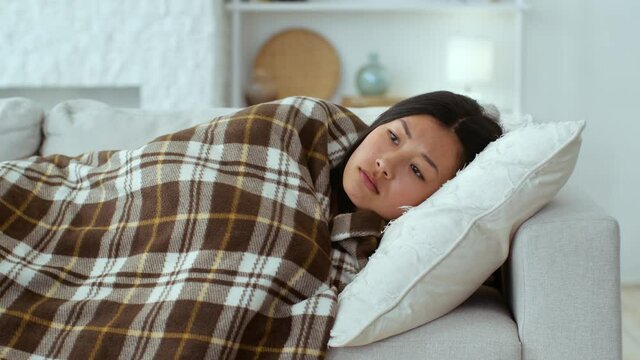 Seasonal depression concept. Young sad asian woman lying on sofa covered with plaid, depressed and unhappy, free space