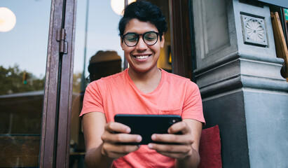 Happy Latin hipster guy in stylish spectacles for provide eyes correction enjoying leisure time for...