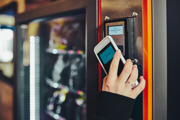Woman paying for product at vending machine using smartphone - obrazy, fototapety, plakaty