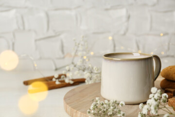Fototapeta na wymiar Cup of hot beverage and flowers on white wooden table, bokeh effect. Space for text