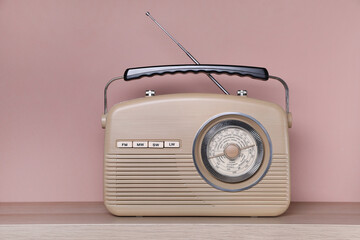 Retro radio receiver on wooden table against pink background