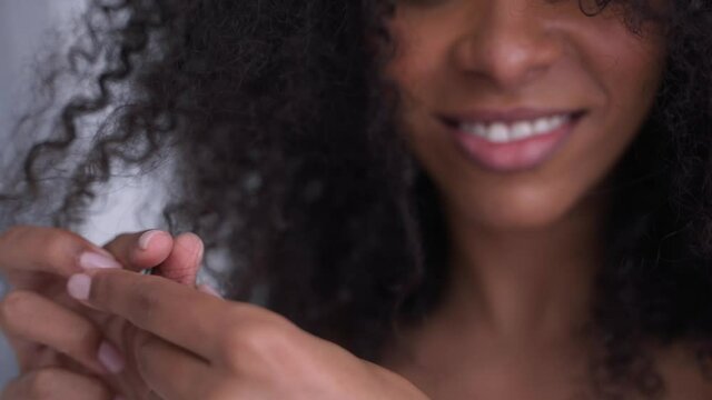 Close-up shot of happy black woman playing with her afro hair in white room. Nature colours of woman hair routine. Dark skin girl smiling and playing with hair. High quality 4k footage