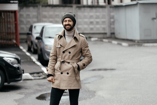 An image of a handsome young bearded man walking down the street and looking at the camera.