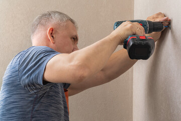 The man drills a hole in the wall. Male hands hold an electric drill to make a hole with a drill. DIY home improvement