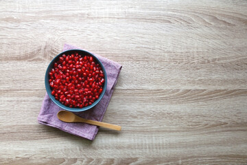 Bowl of fresh pomegranate seeds on wooden table. Top view.