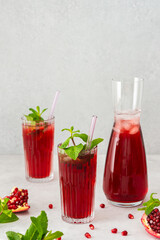 Refreshing pomegranate juice in glasses with mint and glass straw, pitcher of juice and ice, cold drink
