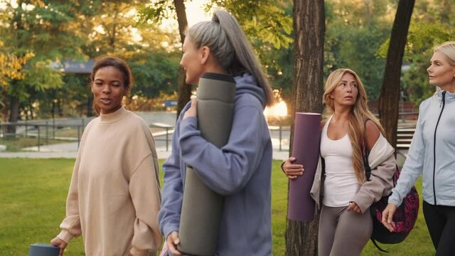 Cheerful multinational mature women going to yoga and talking outdoors