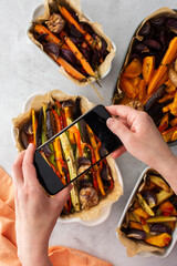 An adult woman takes pictures of stewed vegetables on the phone for social networks or a culinary blog, top view, home cooking hobby, healthy lifestyle
