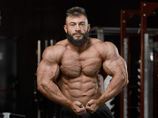 Fototapeta na wymiar Brutal muscular bodybuilder in perfect athletic form posing in the gym. Sport and healthy lifestyle concept