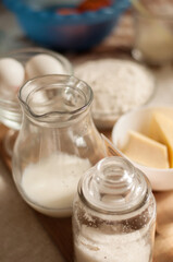 glass jars and a jug with milk and flour with eggs on the background