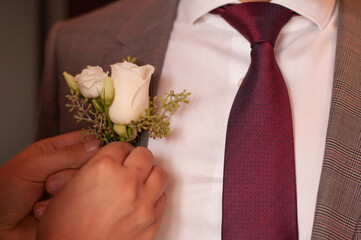 hands attach a boutonniere to the groom's plaid jacket - obrazy, fototapety, plakaty