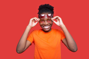 Portrait of a positive African woman in sunglasses on a red background 