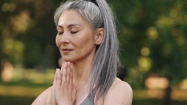 Close-up view of confident Asian mature woman meditating outdoors