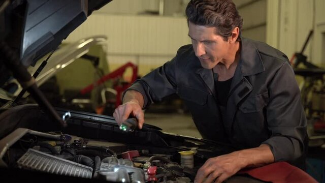 We have a problem. Auto mechanic standing at the opened hood and lighting with lamp while working at the workshop and air filters. Maintenance concept