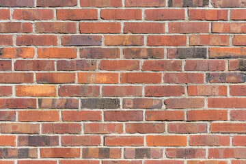 Red brick wall background texture. Multiple rows of weathered stone blocks. Full frame backdrop of a building facade. Rough exterior of a house in aged condition.
