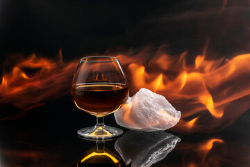 Glass of whiskey with a piece of ice surrounded by flames, concept