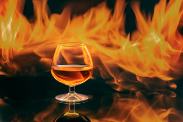 Glass with whiskey with fire and reflections on black background