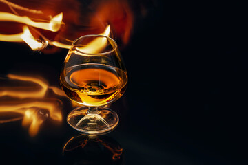 Glass with whiskey with fire and reflections on black background