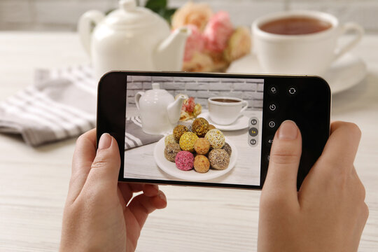 Blogger taking photo of tasty vegan candy balls at white wooden table, closeup