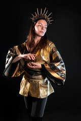 Fototapeta premium A sorceress in a golden shirt in Asian style, a gothic image of a mixture of cultures and styles, a young woman in gold with a crown with rays on her head