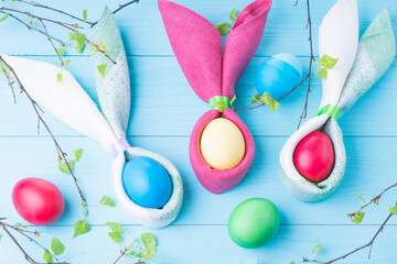 Easter eggs and the shape of rabbit ears and tree branches with green leaves, on a blue wooden background, selective focus, tinted image