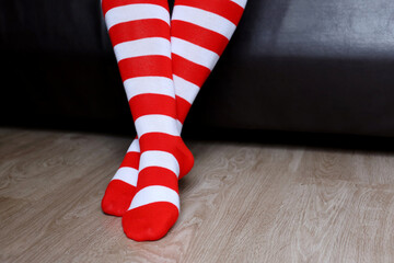 Female legs in Christmas knee socks on a floor, girl sitting on a sofa. Clothing for New Year...