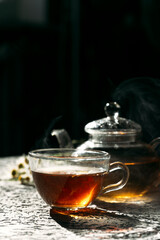 Warm cup of tea with glass teapot on dark background