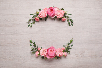 Wreath made of beautiful rose flowers and green leaves on white wooden background, flat lay. Space for text