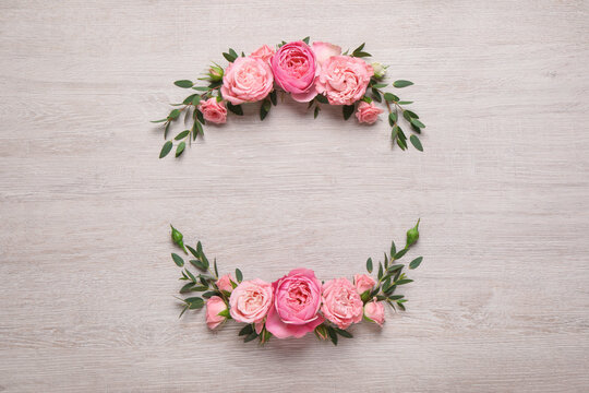 Wreath made of beautiful rose flowers and green leaves on white wooden background, flat lay. Space for text