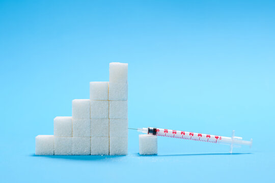 The concept of sugar addiction and the development of diabetes. Sugar cubes and syringe on a blue medical background.