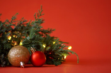 red and gold balls lie next to a green spruce branch on a red background and lights are on
